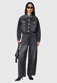 Chaqueta de mezclilla negra cortada con adornos florales, combinada con pantalones de mezclilla negra de pierna ancha y botas de tacón negras.