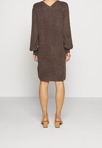 Robe en maille marron avec un col en V, des manches longues bouffantes et une coupe droite, avec un ourlet côtelé. Associée à des sandales à talons blocs camel.