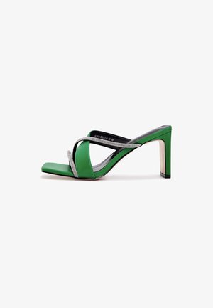 Sandalia de tacón alto verde con punta cuadrada, tiras entrecruzadas con brillantes y tacón delgado, presentada sobre un fondo blanco.
