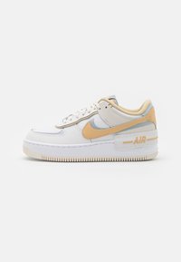 Zapatillas Nike Air Force 1 en cuero blanco con detalles en gris claro y un swoosh naranja pálido. Presentan una suela texturizada y un collar acolchado.