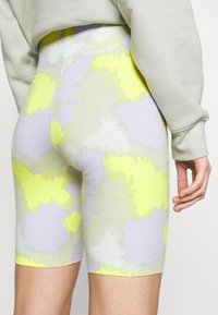 Elastiska shorts i midi-längd i ett mönster av ljus lavendel och neon-gul camouflage. Slät tyg med hög midja och sömlös design.