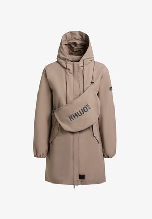 Beige lange jas met capuchon, voorzien van een ritssluiting aan de voorkant en elastische manchetten, gecombineerd met een bijpassende schoudertas met het label "KHUJO 2001".