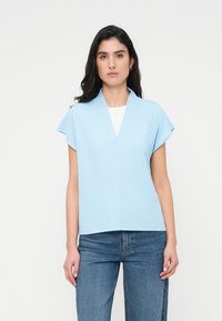Ανοιχτό μπλε κοντομάνικο τοπ με V-λαιμόκοψη και δομημένο γιακά. Απλός σχεδιασμός, λεία υφή και άνετη εφαρμογή, σε συνδυασμό με μπλε τζιν.