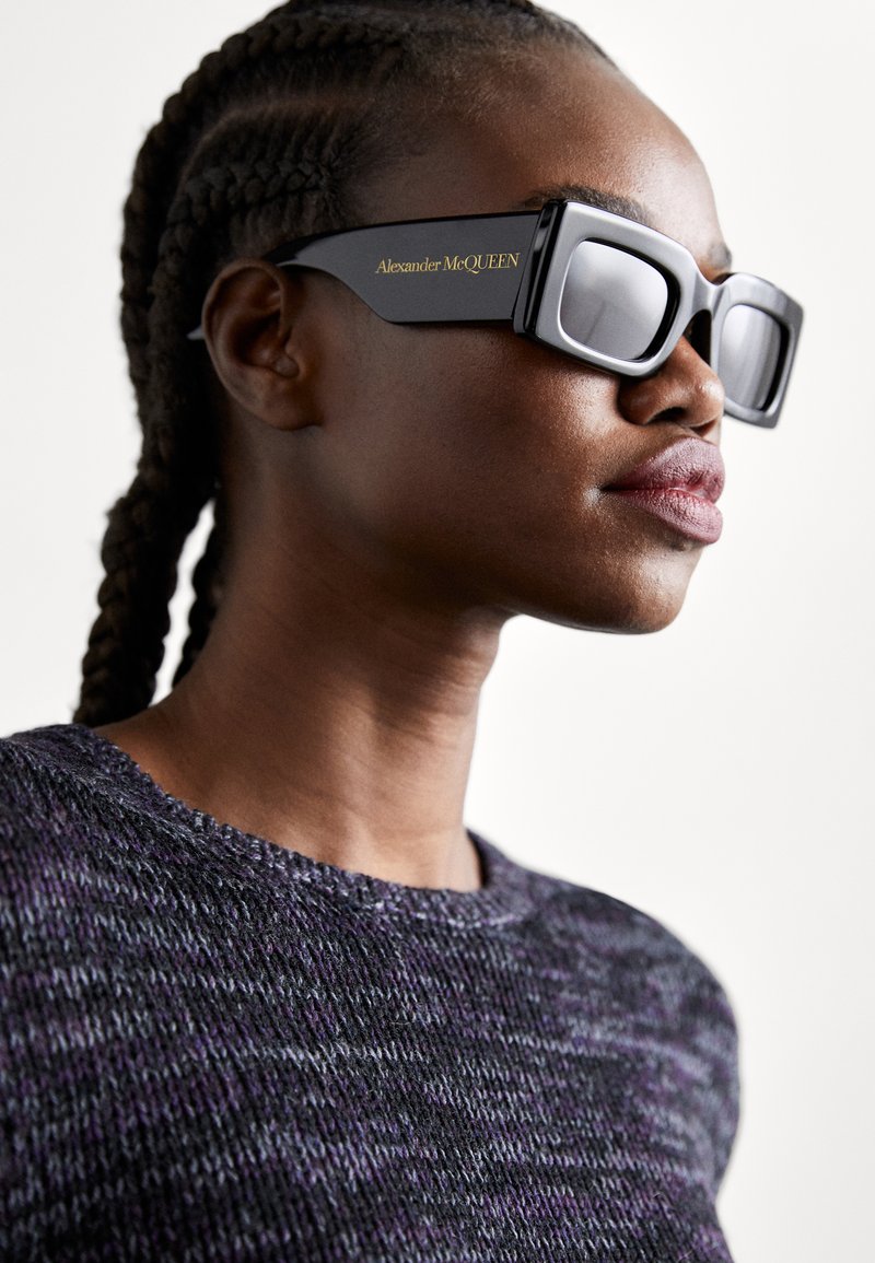Black oversized sunglasses with a rectangular shape, silver reflective lenses, and gold "Alexander McQueen" branding on the frame.