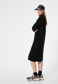 Abito nero a maglia con maniche lunghe, orlo a coste, abbinato a sneakers nere e beige e un berretto in pelle nera.