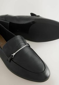 Čierne kožené mokasíny s hladkým povrchom, špicatou špičkou a striebornými kovovými detailmi na hornej časti. Elegantný dizajn a plochá podrážka.