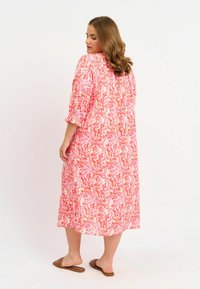 Rosa und korallenfarbenes Midikleid mit abstraktem Muster, dreiviertelärmel und lockerer Passform. Glattes Material und knöchellange Gestaltung.