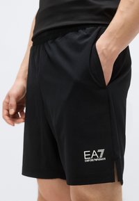 Juodi sportiniai šortai iš lygaus audinio. Turi elastingą juosmenį, šonines kišenes ir logotipo akcentą kairiajame šlaunyje.