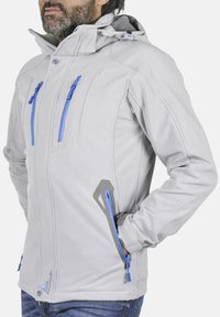 Veste softshell gris clair avec poches zippées bleues, protège-menton et capuche ajustable. Présente des poignets texturés et des designs de poches latérales.