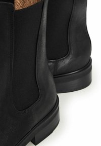Czarne skórzane botki za kostkę z elastycznymi panelami bocznymi i teksturowanym wykończeniem, z niskim obcasem i gładką podeszwą dla lepszej przyczepności.