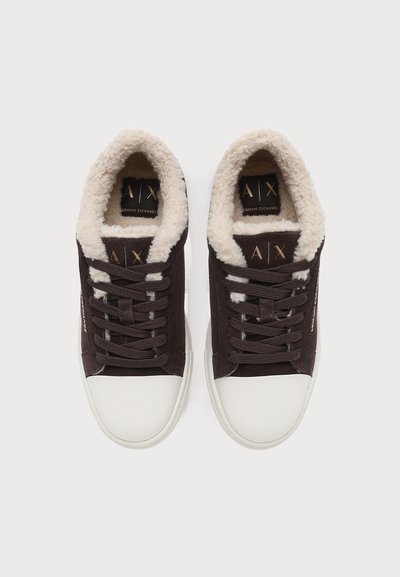Paire de baskets noires à lacets avec bouts en caoutchouc blanc et doublure en polaire blanche, vues de dessus sur un fond uni.