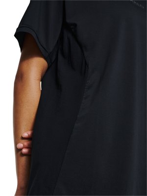 Person trägt ein schwarzes kurzärmeliges Shirt mit einer Hand, die seitlich am Oberkörper anliegt, vor weißem Hintergrund.