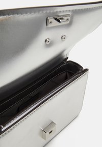 Sac à main en métal argenté avec une texture lisse, de forme rectangulaire, fermeture magnétique et plusieurs compartiments à l'intérieur.