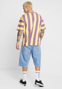 Lila und gelb gestreifes, übergroßes T-Shirt aus Baumwolle, kombiniert mit hellblauen Denim-Shorts mit Gesäßtaschen und Nähdetails.