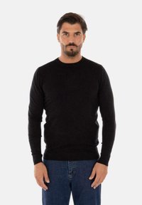 Maglione nero a maglia con scollatura rotonda e maniche lunghe. Presenta polsini e orlo a costine. Abbinato a jeans blu.
