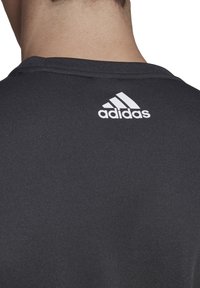 Schwarzes Sport-T-Shirt mit rundem Ausschnitt, kurzen Ärmeln und einem weißen Adidas-Logo auf dem Rücken. Glattes, atmungsaktives Material.