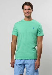 Hele roheline puuvillane T-särk ümmarguse kaelusega ja lühikeste varrukatega, millel on rindkeres väike sinine logo, koos helesiniste lühikesed pükstega.