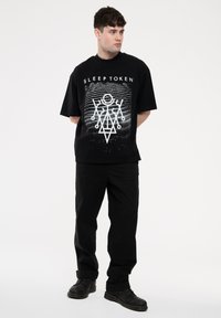 Black graphic t-shirt featuring white text "SLEEP TOKEN" and geometric design, paired with black pants and black shoes. Simple, casual look.