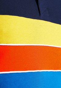 Vícebarevná tkanina s horizontálními pruhy: tmavě modrá, žlutá, oranžová a modrá. Texturovaný, vaflový materiál s kontrastním bílým prošitím.