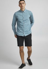 Light blue button-up shirt, long sleeves, made of denim-like fabric. Paired with black shorts and black sneakers. Simple design, no patterns.