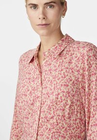 Chemise à boutons florale en rose pâle avec des fleurs de différentes nuances de rose. Tissu léger, col classique et manches longues avec une coupe décontractée.