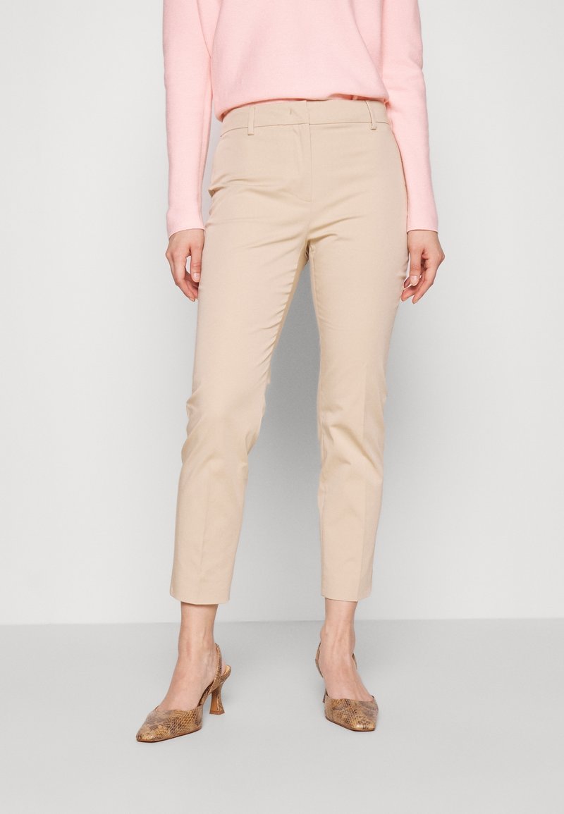 Pantalons beige ajustés avec une coupe slim, longueur cropped et texture lisse, associés à un pull rose clair et des escarpins en imprimé serpent.