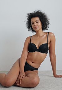 Zwarte lingerieset met een gepadded beha met verstelbare bandjes en bijpassende high-waist slipjes. Gladde textuur met subtiele patroon details.