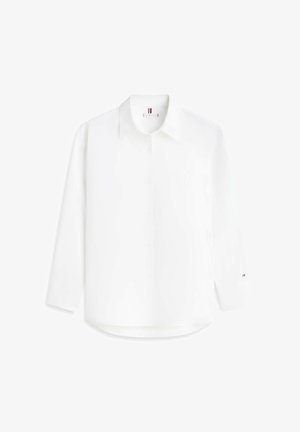 Camisa blanca de manga larga con botones, cuello, logo bordado sutil en el pecho y pequeño logo de bandera en el puño izquierdo.