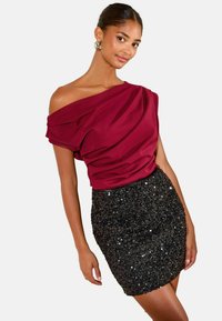 Weinrotes Schulterfreies Oberteil mit drapiertem Stoff, kombiniert mit einem schwarzen Pailletten-Minirock. Glatte Textur, figurbetontes Design und funkelnde Akzente.
