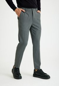 Grijze op maat gemaakte broek met een subtiele textuur, voorzien van een knoopsluiting, zijzakken en een enkellange pasvorm, gecombineerd met zwarte sneakers.