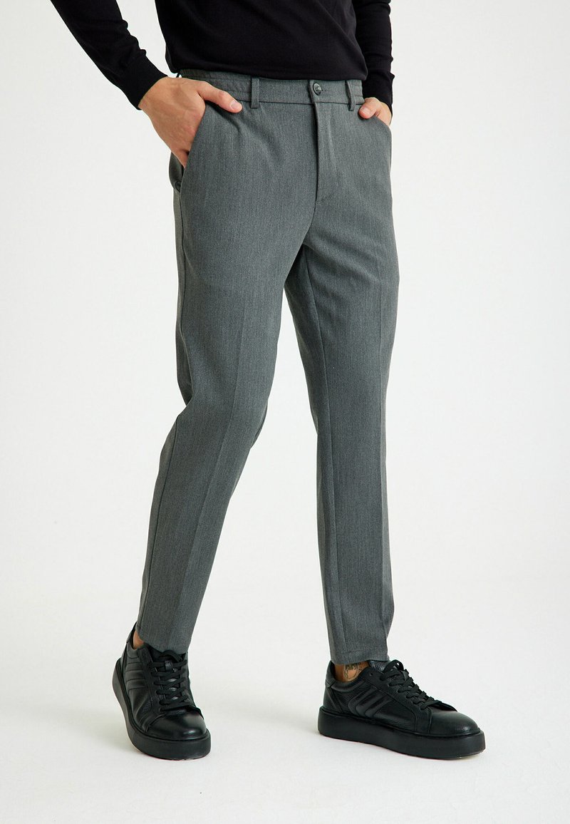 Grijze op maat gemaakte broek met een subtiele textuur, voorzien van een knoopsluiting, zijzakken en een enkellange pasvorm, gecombineerd met zwarte sneakers.