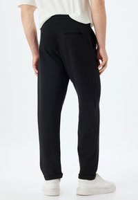Pantalones de chándal negros hechos de una tela suave, con un corte relajado, cinturilla elástica y un bolsillo trasero. Estilizados con puños enrollados y zapatillas blancas.