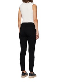 Zwarte getailleerde broek met een gladde textuur en een gemiddelde taille, voorzien van twee achterzakken, gedragen met een witte mouwloze top en sneakers.