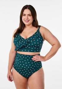 Mörkgrön bikinitopp med prickar och volangdetaljer samt högmidjade bottnar. Materialet verkar elastiskt och slätt.