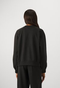 Felpa nera realizzata in morbido tessuto con scollatura rotonda e polsini a coste. Presenta una vestibilità comoda e un design semplice.