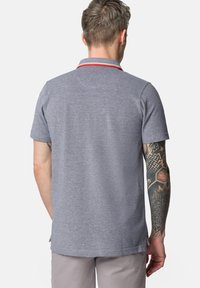 Szary polo z krótkim rękawem, z paskowanym kołnierzykiem i czerwonymi akcentami. Posiada prosty dół i subtelną teksturę. Noszony przez osobę z tatuażami.