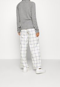 Graues, eng anliegendes Langarmoberteil, kombiniert mit lockeren weißen Hosen mit einem blauen Karomuster. Weiße Sneaker runden das Outfit ab.