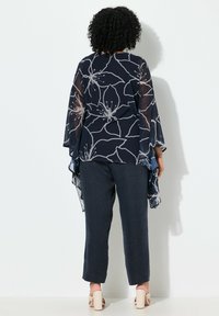Navy floral blouse with sheer sleeves, featuring a light floral pattern, paired with textured dark pants and beige heeled sandals.