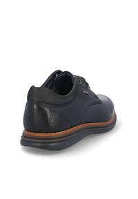 Zapato de cuero negro con un acabado texturizado, suela de goma marrón y costuras en contraste. Diseño con cordones, cuello acolchado y detalle de marca.