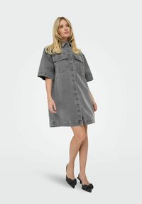 Grå denimklänning med korta ärmar, knäppning framtill, två bröstfickor och avslappnad passform. Matchas med svarta klackskor med rosett.