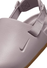 Lähedalt vaade lavendlivärvilisele Nike sandlele, millel on reguleeritavad kangastrapid ja tekstureeritud kummitald.
