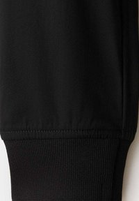 Manche en tissu noir avec un bord-côtes en bas, montrant les détails des coutures et le contraste de texture entre le matériau lisse et tricoté.