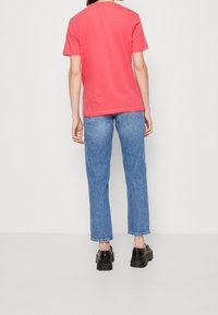Korálová bavlněná trička s krátkými rukávy, kombinovaná se světle modrými rovnými džíny a černými platformovými botami. Zadní pohled ukazuje střih oděvu.