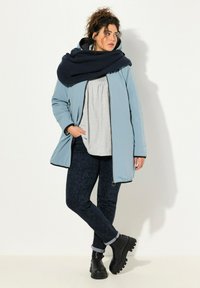 Světle modrá péřová bunda s námořnickou pletenou šálou, šedým topem, vzorovanými tmavě modrými kalhotami a černými robustními kotníkovými botami.