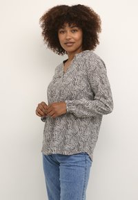 Langärmliges Oberteil in Schwarz und Weiß mit einem wellenförmigen Muster, V-Ausschnitt und lockerer Passform, kombiniert mit hellblauen Jeans.