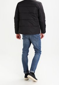 Svart vadderad jacka med horisontell sömnad, i kombination med blå jeans och svarta högskurna sneakers. Enkel, strömlinjeformad design.