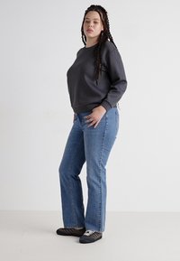 Szürke pulóver, kerek nyakkivágással, kék bővülő farmernadrággal párosítva. A modellen fekete-fehér csíkos tornacipő van.