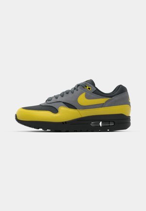 Gray and yellow sneaker with a mesh and suede upper, lace closure, black midsole with visible air unit, and textured rubber outsole.