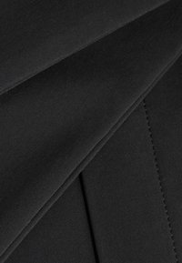 Närbild av svart tyg med lager av veck och synlig söm detaljer på en slät textilyta.