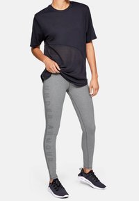 Czarna koszulka z krótkim rękawem z siateczki, szare legginsy z napisem "Under Armour" i czarne buty sportowe; nowoczesny strój sportowy z kontrastującymi kolorami.